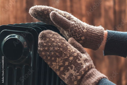 Women's hands in Christmas, warm, winter mittens on the heater. Keep warm in the winter, cold evenings