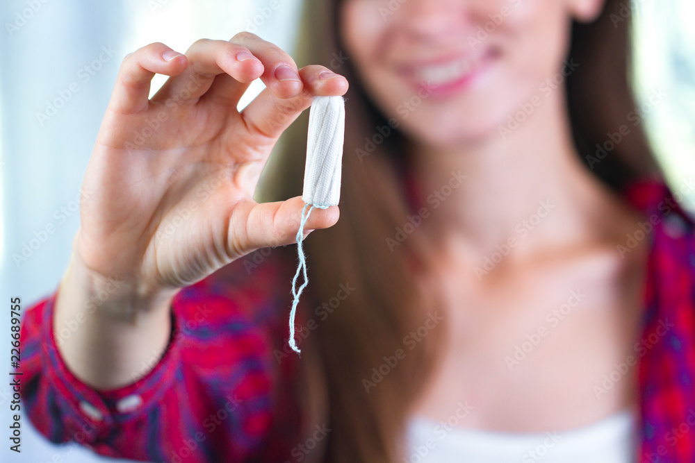 Fototapeta premium Attractive young woman holding a tampon. Critical days. Women's and gynecological health care. Hygiene. Menstrual cycle. Hygiene care during critical days. Tampon woman