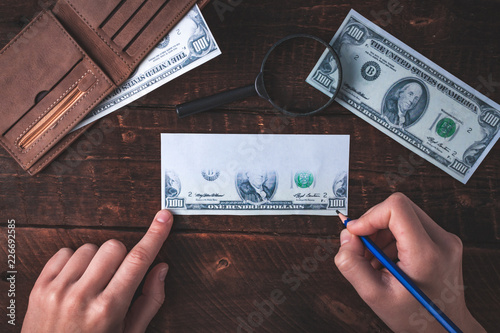 Counterfeiter forges banknotes. Fake concept. Fake money, a wallet with American dollars, a magnifier on a wooden background. Top view
