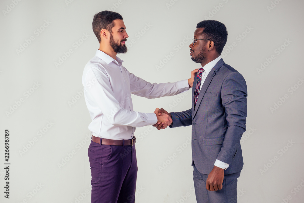 male businessman and his Aro-American partner shaking hands in the studio on a white background