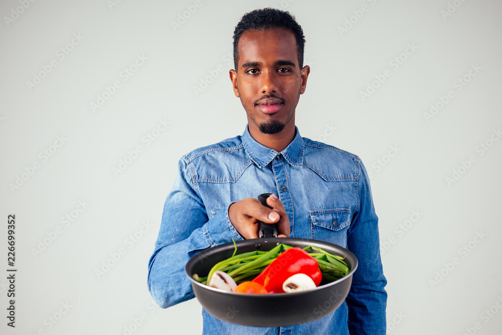 african american chef kitchener holding a frying pan wizard man cooking magic flying food salad, carrot, garlic, onion, pepper, potato, cucumber isolate white background studio.magic of taste fantasy african american chef kitchener holding a frying pan wizard man cooking magic flying food salad, carrot, garlic, onion, pepper, potato, cucumber isolate white background studio.magic of taste fantasy