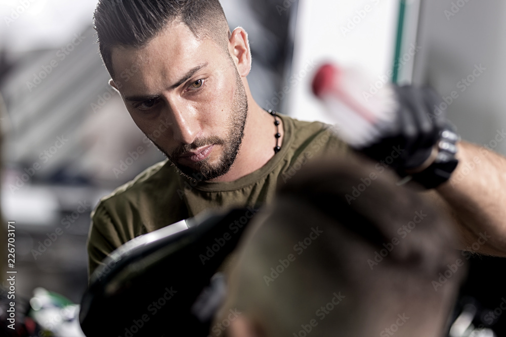 Handsome barber dries hair and makes a styling of dark-haired man at a barbershop Handsome barber dries hair and makes a styling of dark-haired man at a barbershop