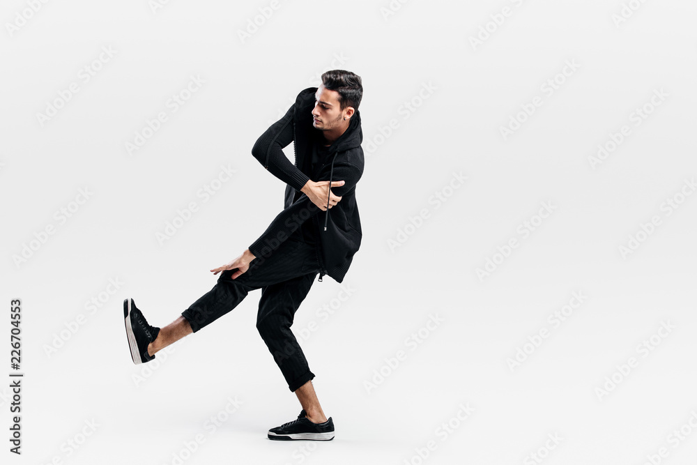 Young dancer dressed in a stylish black clothes lifts one leg up while dancing street dance