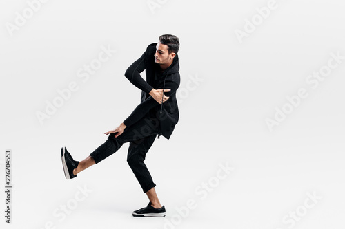 Young dancer dressed in a stylish black clothes lifts one leg up while dancing street dance