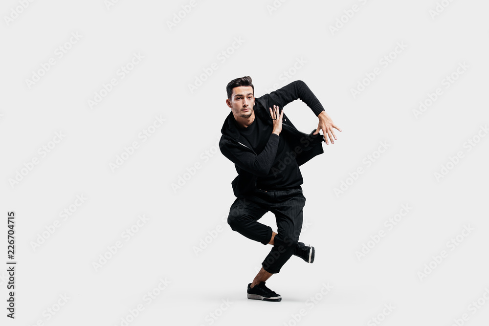 Stylish young man wearing a black sweatshirt and black pants makes stylized movements of hip-poh Stylish young man wearing a black sweatshirt and black pants makes stylized movements of hip-poh