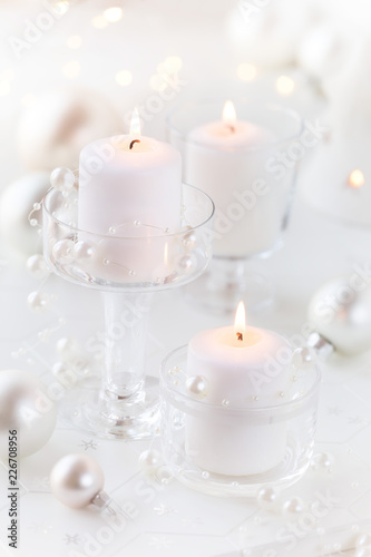 Lit white candles in transparent glass candle holders with festive Christmas decorations at the background