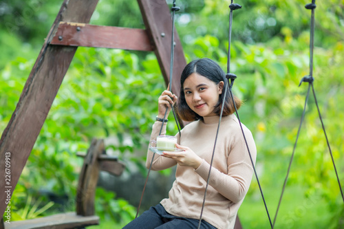 Asian girl on wooden swing and enjoy with her green tea