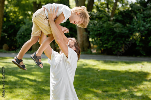 Sunny summer day. Cheerful father lifted his little son up above himself and tickling him.