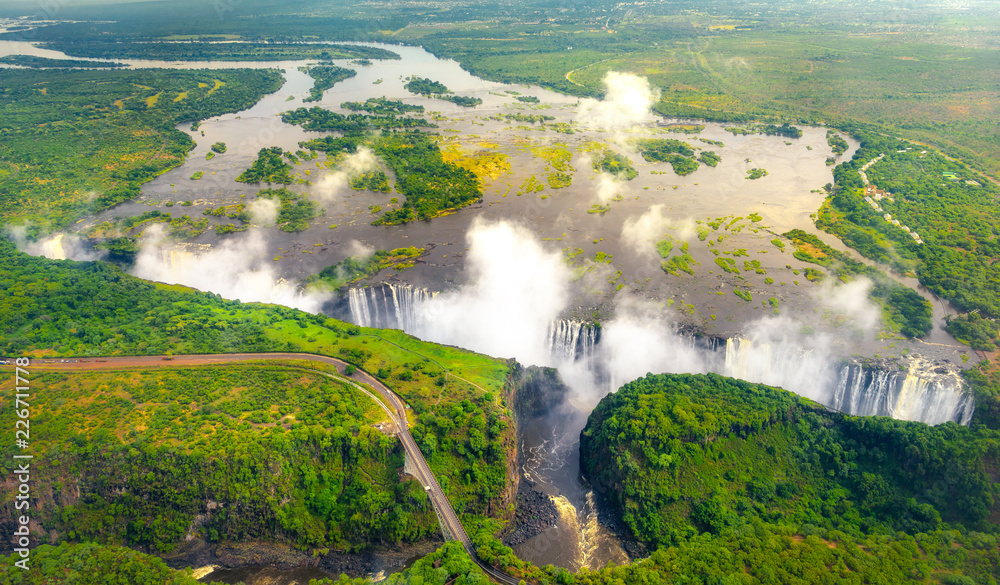 Fototapeta premium Wodospady Wiktorii w Zimbabwe i Zambii, zdjęcie z helikoptera z lotu ptaka, zielony las wokół niesamowitych majestatycznych wodospadów Afryki. Livingston Bridge nad rzeką