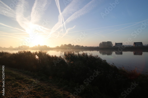 Sunrise with colored aircraft trails, fog on the meadows and dyke at River Hollandsche IJssel in the Netherlands at nieuwerkerk. photo