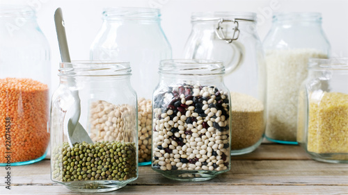 Various cereals, grains and beans in glass jars. Lentils, chickpeas, peas, beans, quinoa, rice and bulgur. Concept  Clean eating. White background and wooden table
