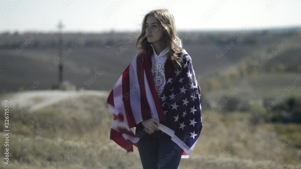 A young beautiful girl is holding a USA flag, which is developing in the wind. A young beautiful girl is holding a USA flag, which is developing in the wind.