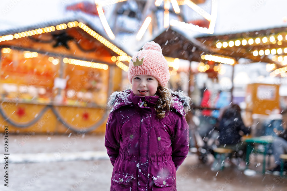 Little cute kid girl having fun on traditional German Christmas market during strong snowfall.
