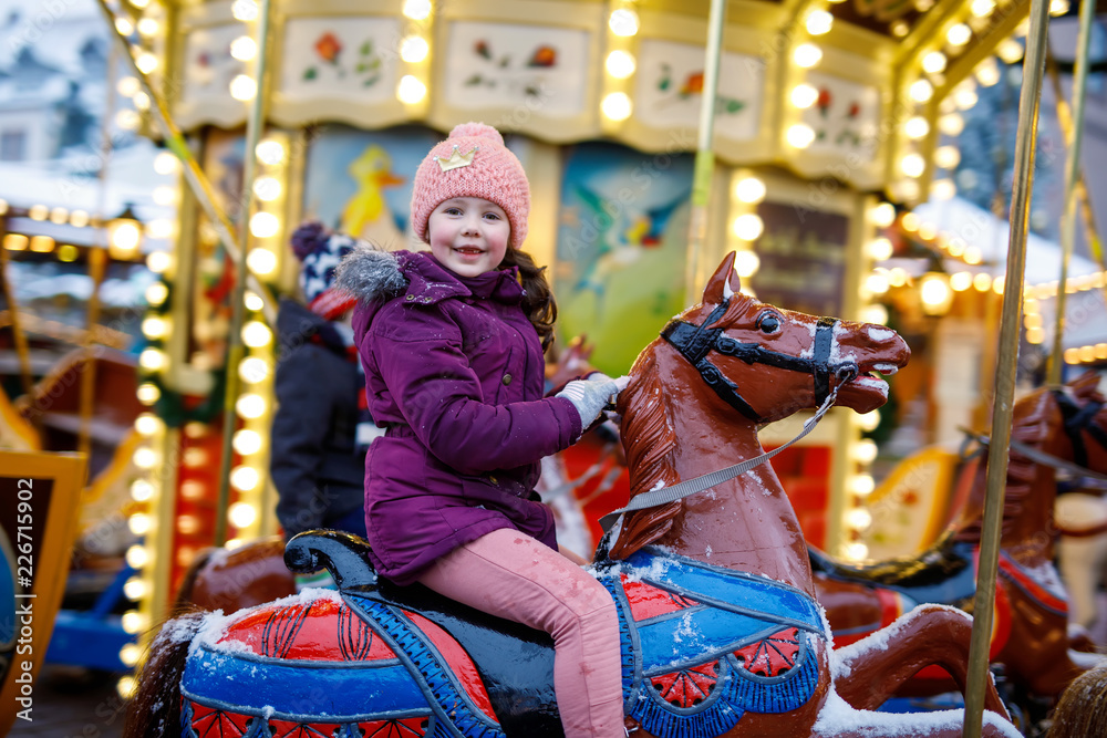 Adorable little kid girl riding on a carousel horse at Christmas funfair or market, outdoors.