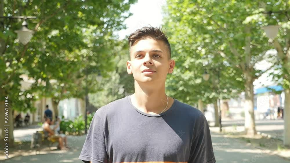 Portrait of a cheery young man with a short haircut in a T-shirt walking in a green park alley being happy on a sunny day in slow motion Portrait of a cheery young man with a short haircut in a T-shirt walking in a green park alley being happy on a sunny day in slow motion