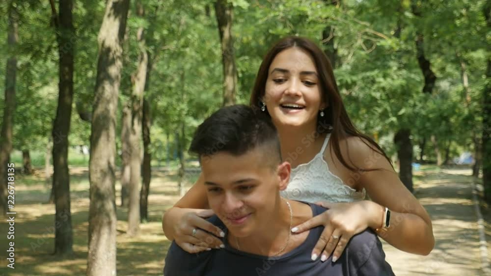 Jolly view of a couple in love frolicking and smiling in a green forest in summer. A gorgeous girl jumps on her boy`s back in summer Jolly view of a couple in love frolicking and smiling in a green forest in summer. A gorgeous girl jumps on her boy`s back in summer