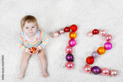 Adorable baby girl holding colorful vintage xmas toy ball in cute hands. Little child and Christmas tree balls as twelve.