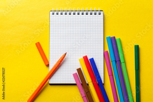 Felt-tip pens and blank notepad on bright yellow background