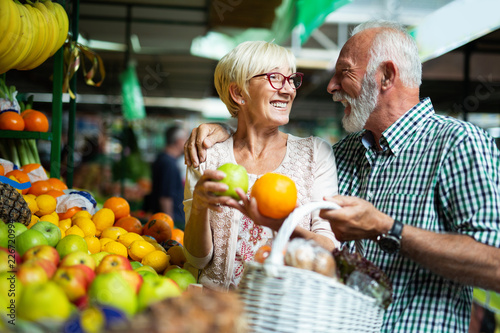 Smiling senior couple holding basket with vegetables at the market