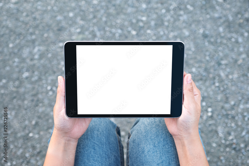 Top view mockup image of a woman holding black tablet pc with blank white screen while sitting on the street background