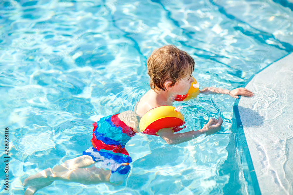 Happy little kid boy having fun in an swimming pool. Active happy child learning to swim. with safe floaties or swimmies. Family, vacations, summer concept