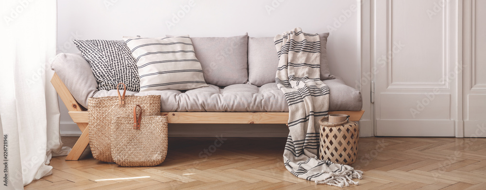 Panorama of pillows and blanket on wooden beige couch in white flat interior with door. Real photo - obrazy, fototapety, plakaty 