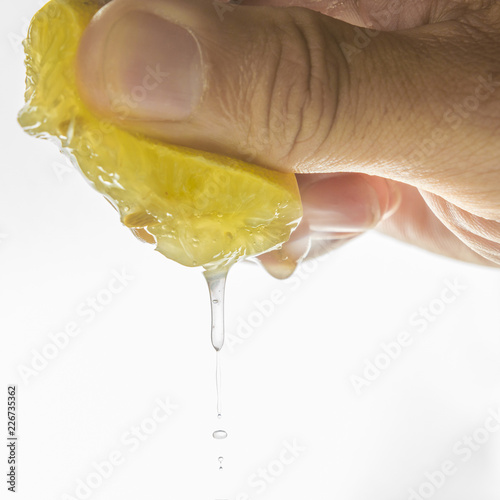 close up Human hand squeezing half of lemon on white background