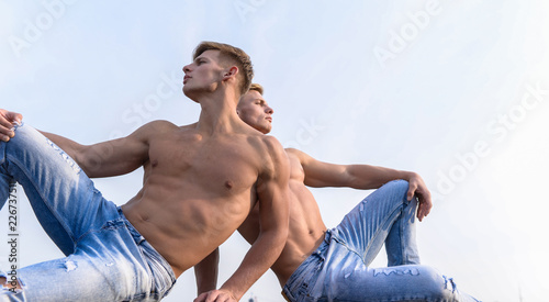 Divine beauty. Sexy torso attractive body. Denim pants emphasize masculinity sexuality. Men twins brothers muscular guys sit relax sky background. Men strong muscular athlete bodybuilder relaxing