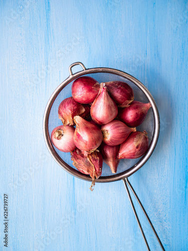 Shallots in the colander on a blue wooden background