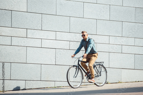 handsome stylish man in sunglasses riding bicycle on street