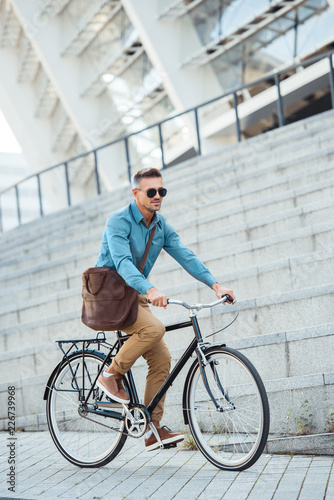 handsome middle aged businessman in sunglasses riding bike on street