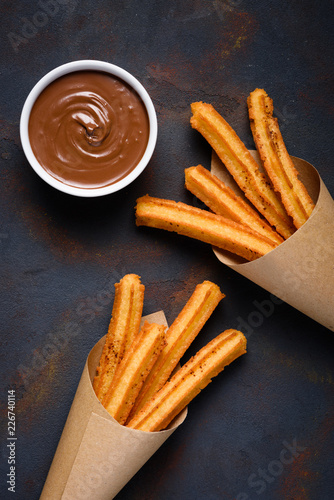 Churros with cinnamon and chocolate sauce on dark background flat lay top view