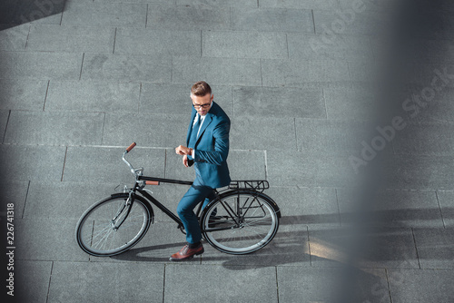 high angle view of businessman in formal wear sitting on bike and checking wristwatch