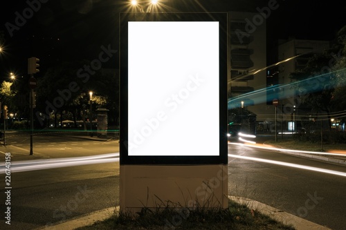 Light box with white blank space for advertisement at road intersection. Night street urban mockup concept with car light trails. 