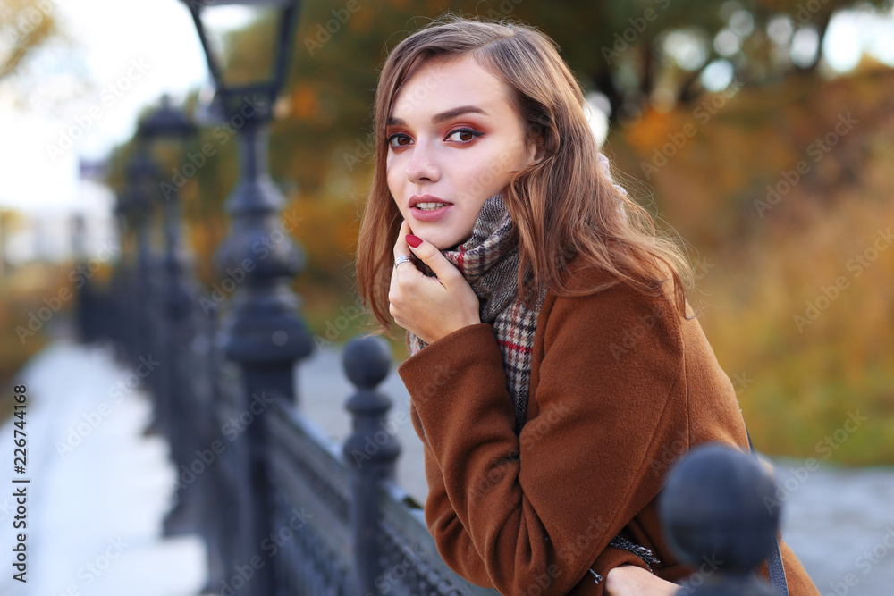 Fashion young woman outdoor. Wearing coat, scarf, and handbag