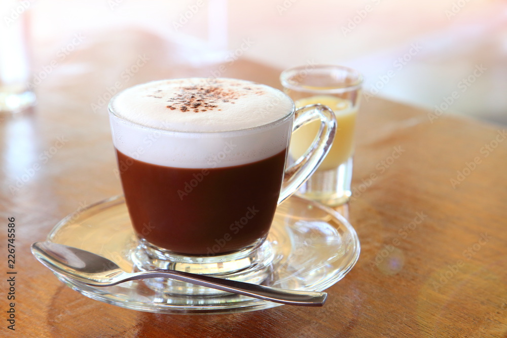 A cup of hot chocolate with foam on top and a shot of sweetened condensed milk on wooden table in the cafe A cup of hot chocolate with foam on top and a shot of sweetened condensed milk on wooden table in the cafe
