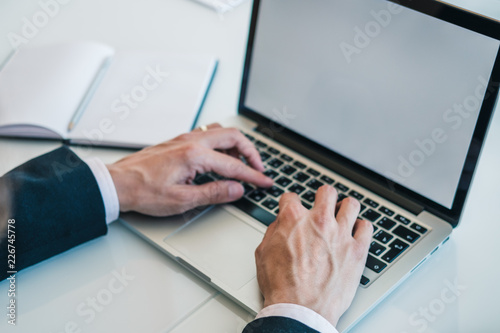 Businessman in black suit and white shirt using laptop for work at office. Concept of using technology for work. Horizontal.