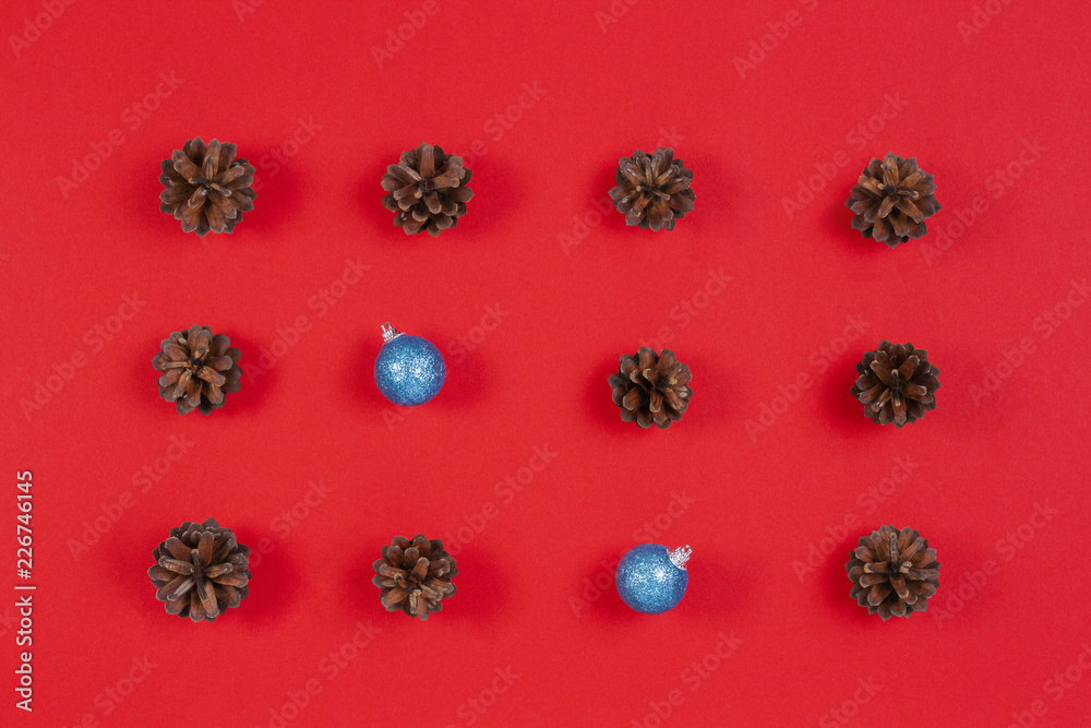 Christmas composition. Pattern made of pine cones and blue christmas decoration on red background. Top view, flat lay Christmas composition. Pattern made of pine cones and blue christmas decoration on red background. Top view, flat lay