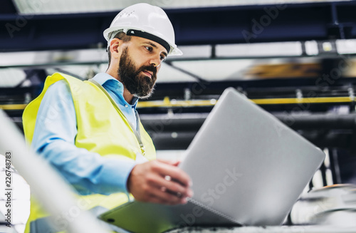 A portrait of an industrial man engineer with laptop in a factory, working. photo