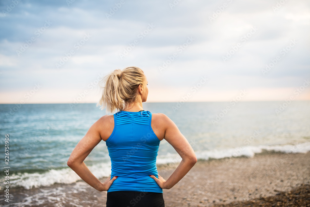 Rear view of young sporty woman runner in blue sportswear standing on the beach. Rear view of young sporty woman runner in blue sportswear standing on the beach.