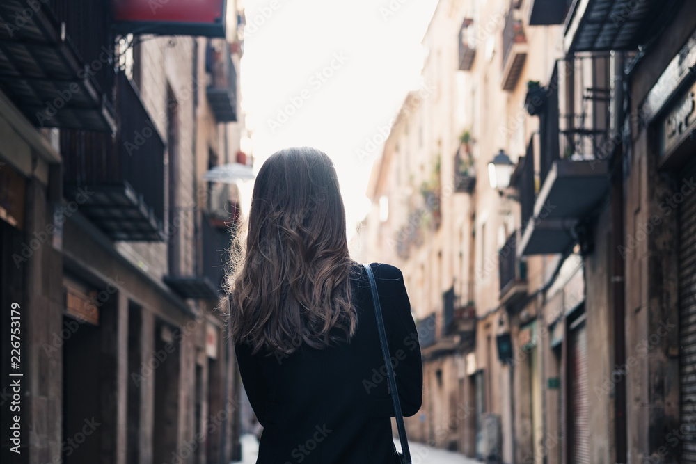 Beautiful girl in black coat walking down the narrow street, exploring the old town. Touristic concept. Horizontal