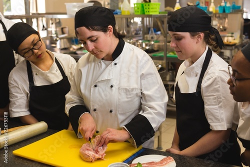 Female chef cutting meat on chopping board in kitchen