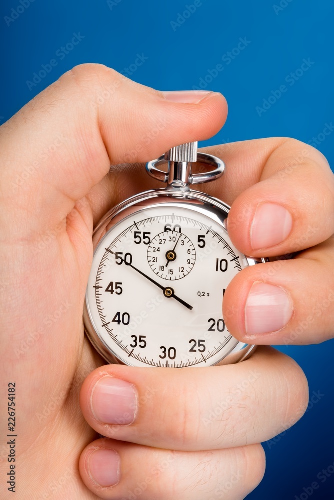 Close Up Of Hand Holding Stopwatch on Blue Blackground Close Up Of Hand Holding Stopwatch on Blue Blackground