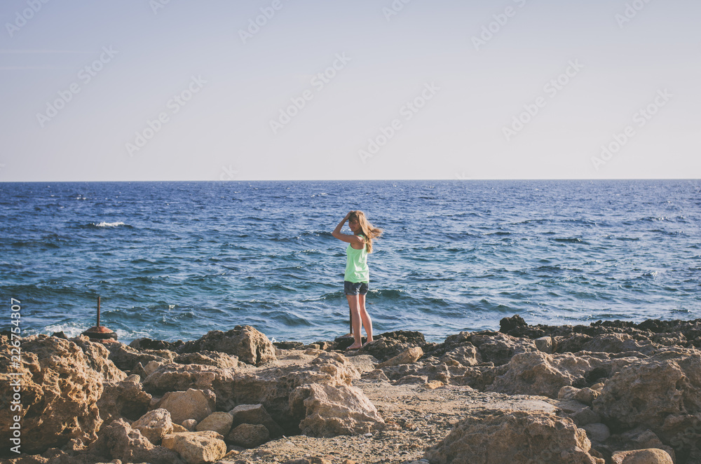 A woman stands on the beach near the ocean and looks at the rolling waves