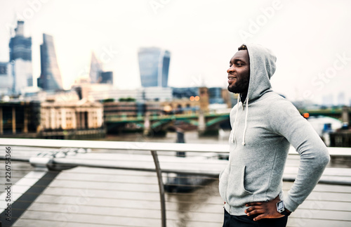Black man runner with smart watch standing on the bridge in a city, resting.