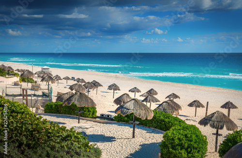 Cancun beach in mexico with umbrellas in the sand, beautiful blue water with dramatic clouds