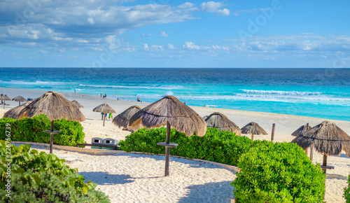 Cancun beach in mexico with umbrellas in the sand, beautiful blue water with dramatic clouds