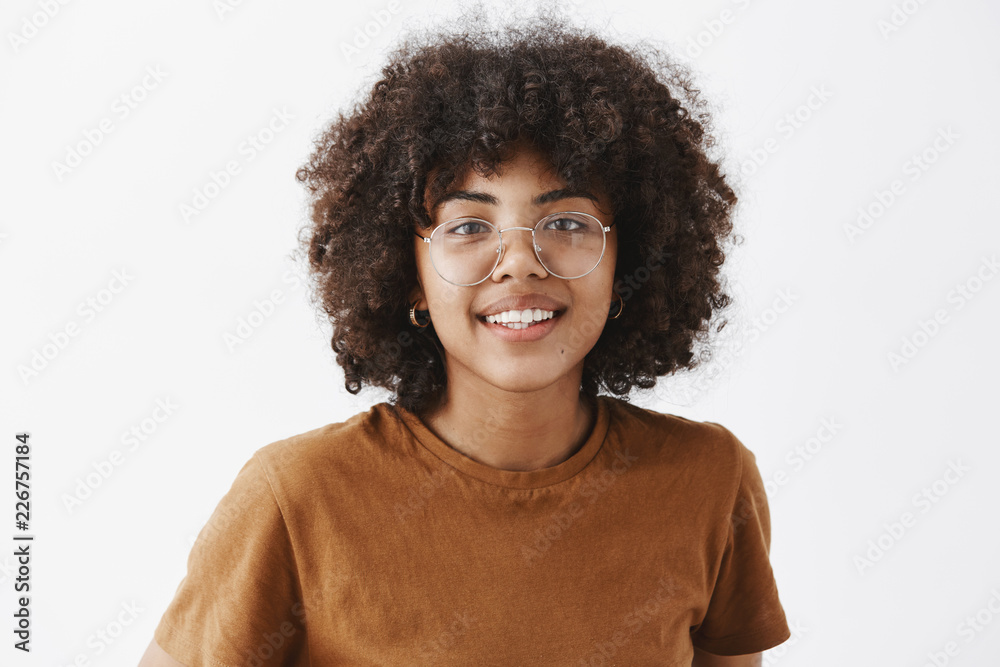 Close-up shot of friendly good-looking african american female student in transparent glasses and brown t-shirt smiling with joyful pleasant smile being satisfied with how things going over gray wall Close-up shot of friendly good-looking african american female student in transparent glasses and brown t-shirt smiling with joyful pleasant smile being satisfied with how things going over gray wall