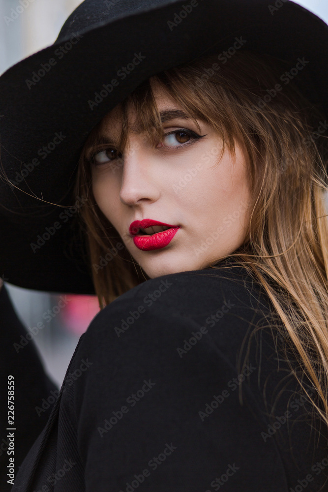 Street portrait of luxurious young model with reg lips wearing black hat and jacket Street portrait of luxurious young model with reg lips wearing black hat and jacket