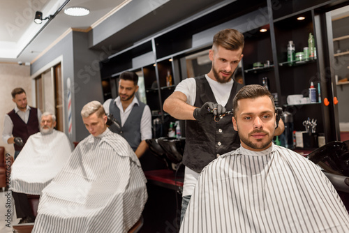 Concentrated hairdresser making professional and stylish haircut to client.